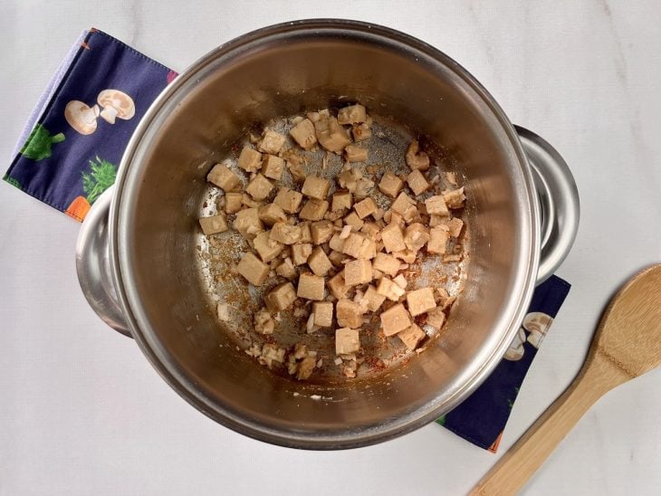 Uma panela refogando cebola, alho e tofu.