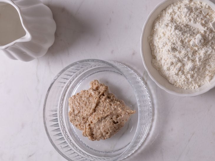 Um recipiente com uma porção do fermento, farinha e água sobre a bancada.
