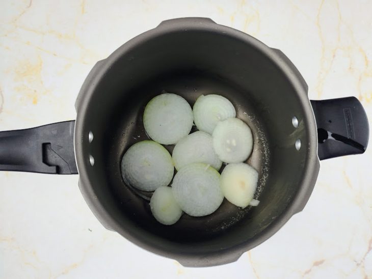Na panela de pressão, o óleo e as rodelas de cebola.