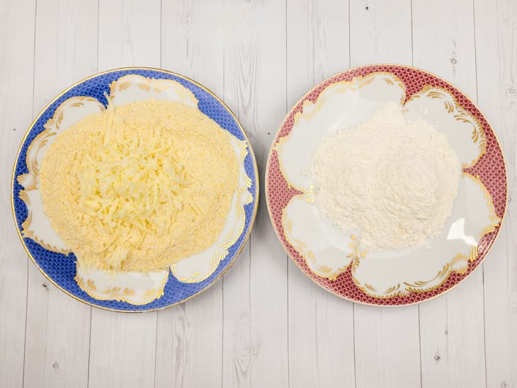 Uma bancada com dois pratos contendo farinha de rosca com queijo e outro com farinha de trigo.