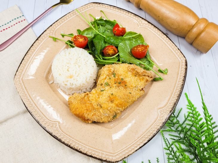 Um prato contendo arroz, folhas e filés de frango à milanesa.