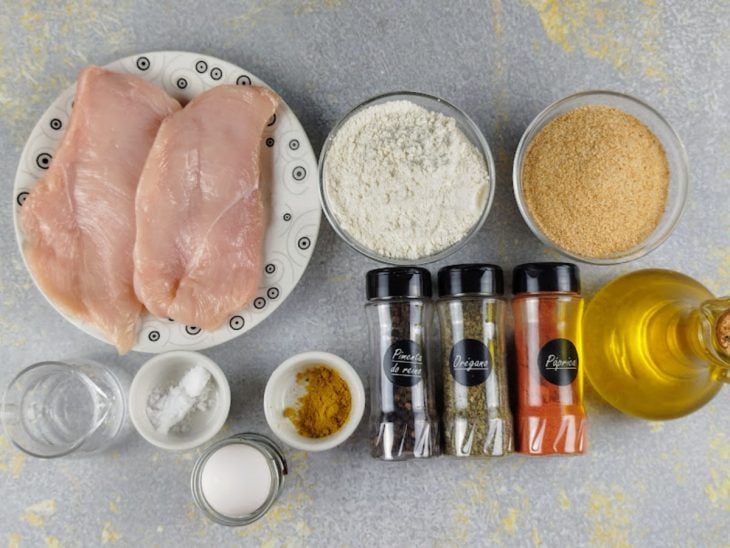 Ingredientes para a receita de filé de frango empanado reunidos em uma bancada.