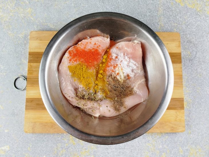 Filés de frango em um recipiente redondo com temperos adicionados.