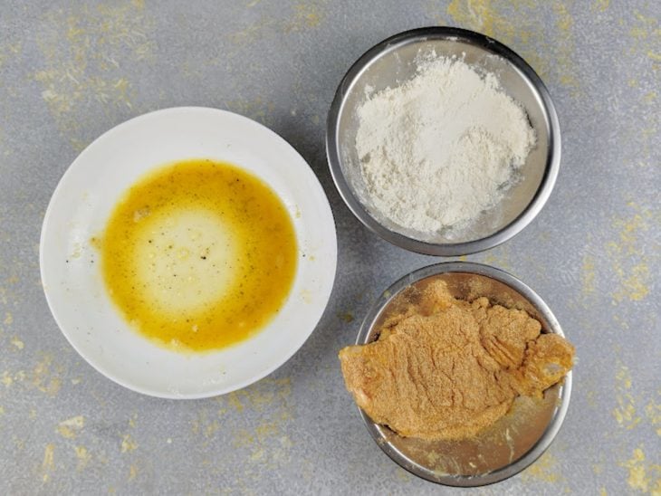 Filé de frango no recipiente com farinha de rosca.