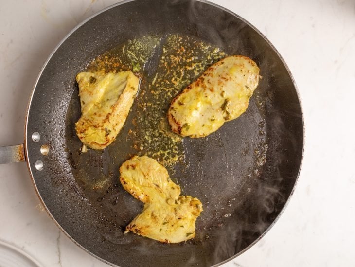 Filés de frango grelhando em uma frigideira com azeite e manteiga.