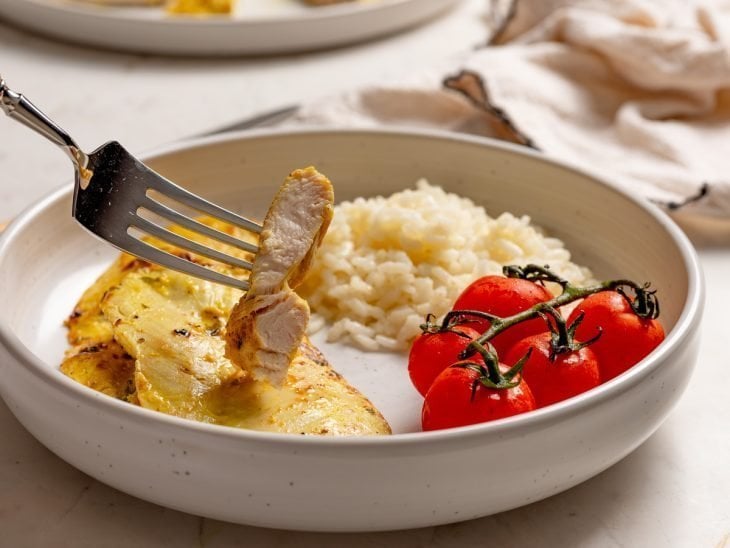 Filé de frango pronto para consumo em um prato com arroz e tomatinhos.