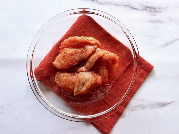 Filés de frango temperados em uma vasilha transparente.