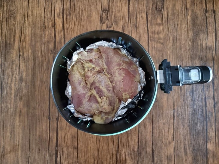 Uma cesta de air fryer com filés de frango crus sobre papel alumínio.