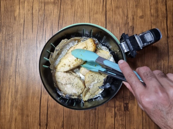 Uma cesta de air fryer com filés de frango quase no ponto certo de cozimento.