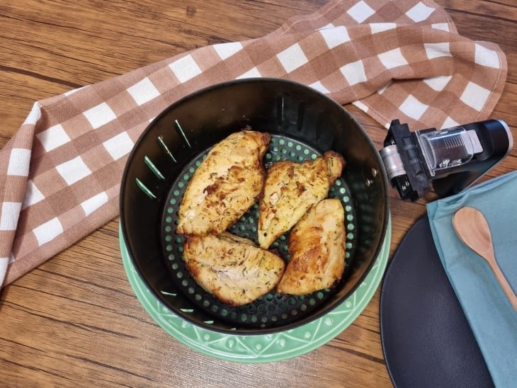 Uma cesta de air fryer com 4 filés de frango assados.