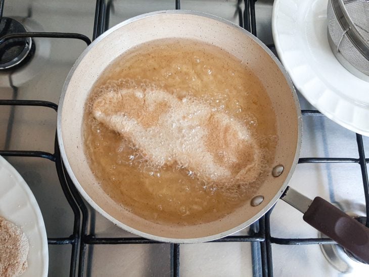 Filé empanado sendo frito em uma frigideira com óleo.