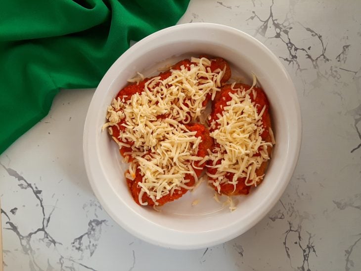 Refratário com filés empanados com molho e queijo ralado.