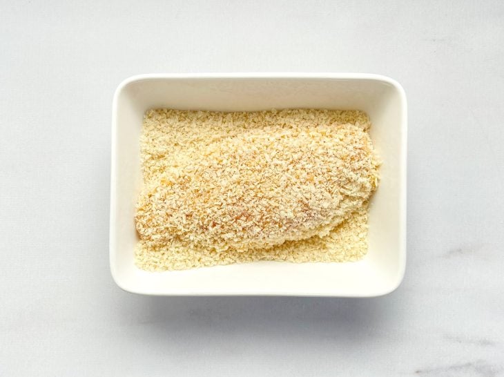 Um recipiente contendo farinha panko empanando um filé de frango recheado.