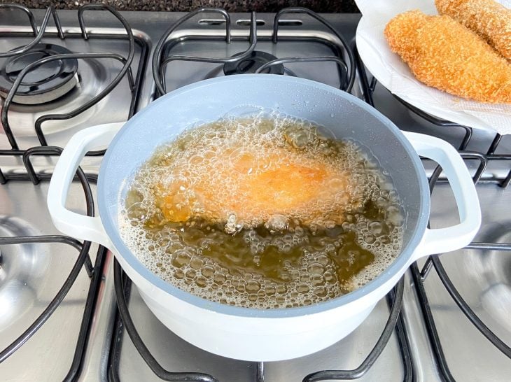 Uma panela contendo óleo quente fritando o filé de frango recheado.