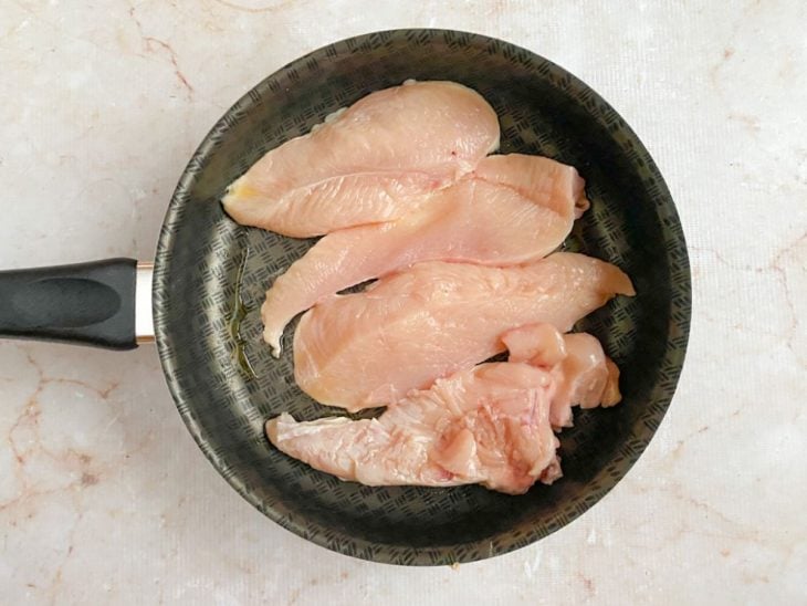 Filés de frango em uma frigideira com azeite.