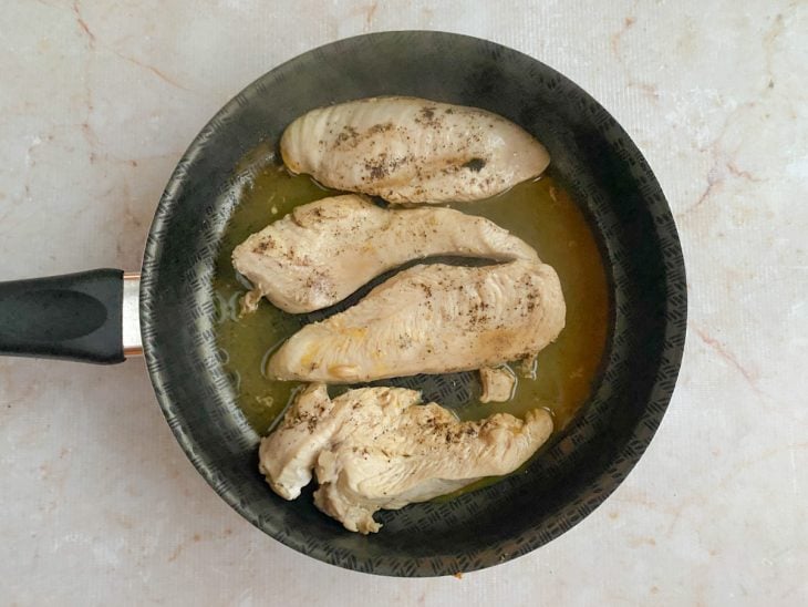 Sal, pimenta-do-reino e suco de limão adicionados à frigideira para temperar os filés de frango.