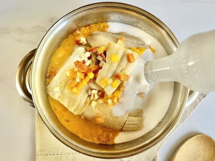 Leite de coco sendo adicionado na panela com os filés de peixe e os outros ingredientes.