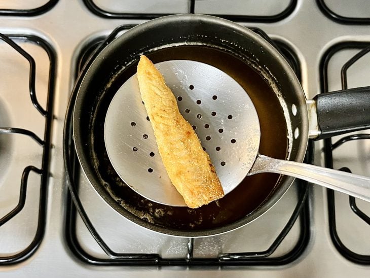 Uma panela com óleo quente e um filé de panga frito.
