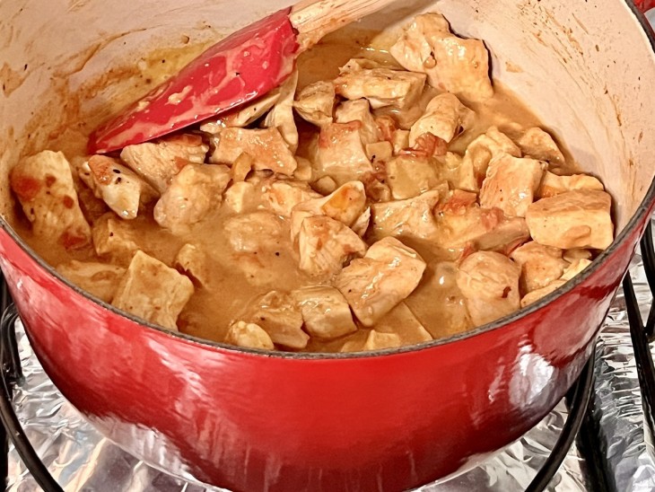 Uma panela contendo cubos de frango com leite de coco.