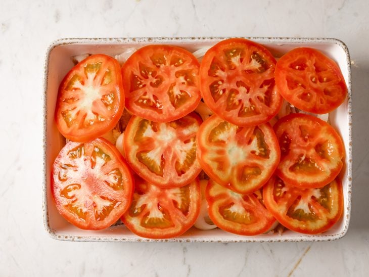 Um refratário com as camadas do filé de peixe, batatas e tomates.