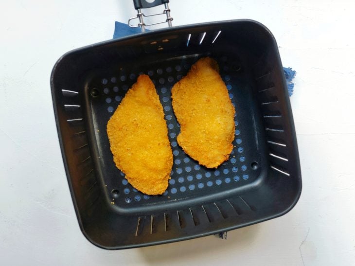 Uma cesta de airfryer contendo dois filés de peixe empanados.
