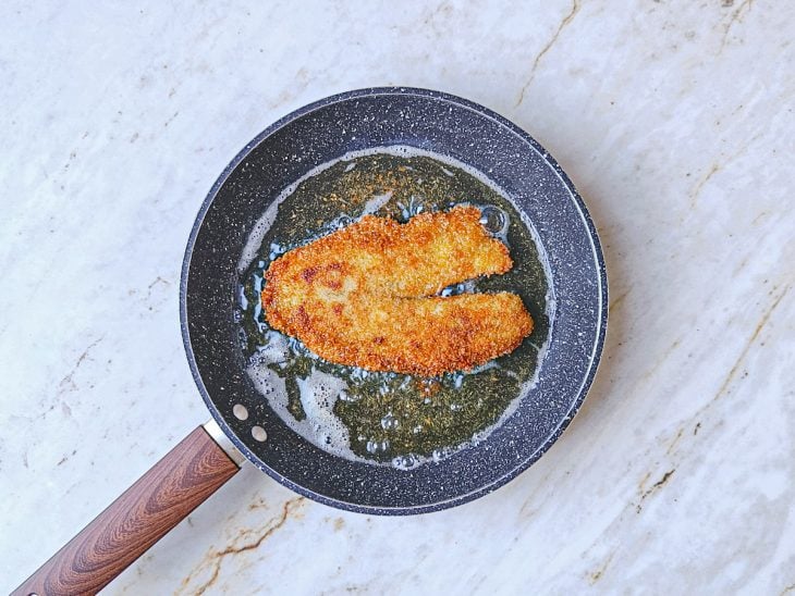 Filés empanados fritando em frigideira com óleo.