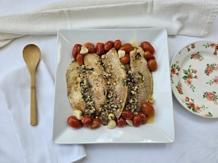 Um prato contendo filés de tilápia com tomate confit e molho de castanha.