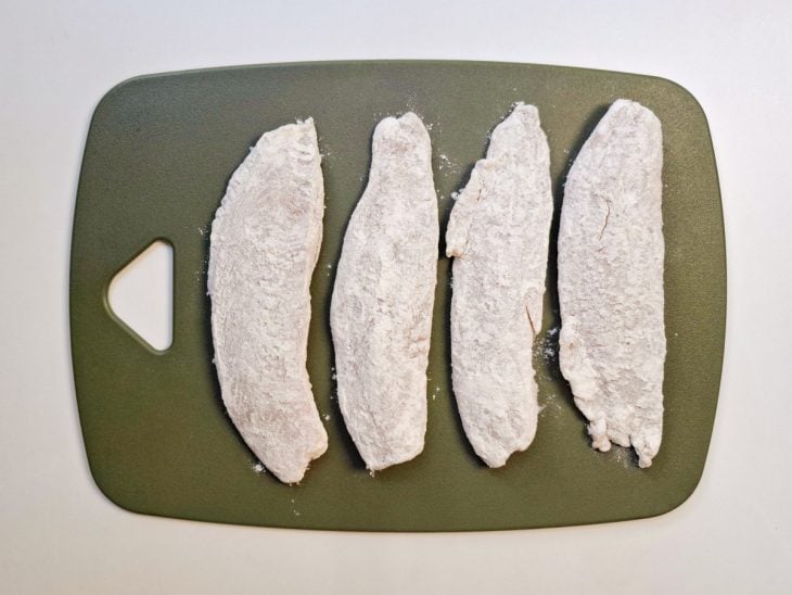 Uma tábua com os filés empanados com a farinha de trigo.