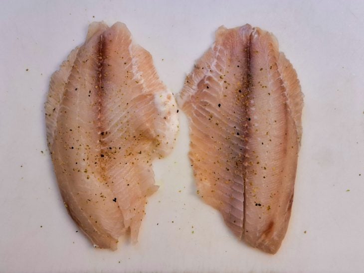 Filés de tilápia sobre uma tábua temperados com sal e lemon pepper.