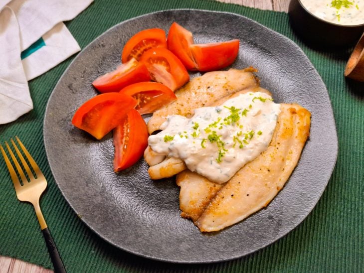Prato composto por filés de tilápia com molho de limão e tomates picados ao lado.