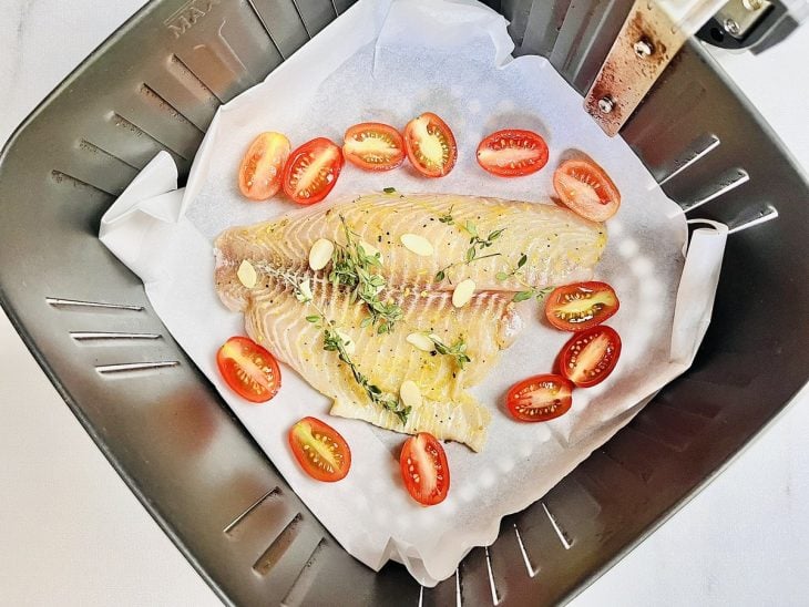 Filé temperado com tomatinhos, tomilho e alho acomodados no cesto da air fryer forrado com papel manteiga.