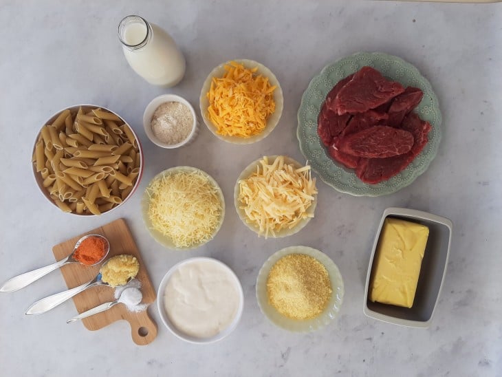 Ingredientes reunidos: carne, queijos, temperos, leite, manteiga, macarrão, farinha, creme de leite e alho.