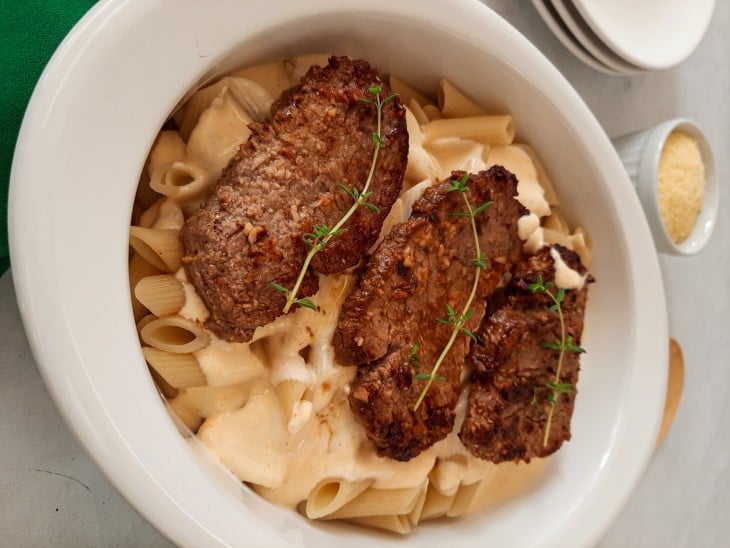 Travessa preenchida com o macarrão, o molho de 4 queijos e os medalhões de filé mignon.