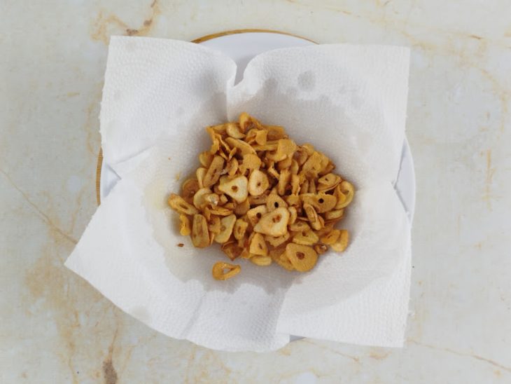 Lâminas de alho sendo fritas em óleo quente até dourar.