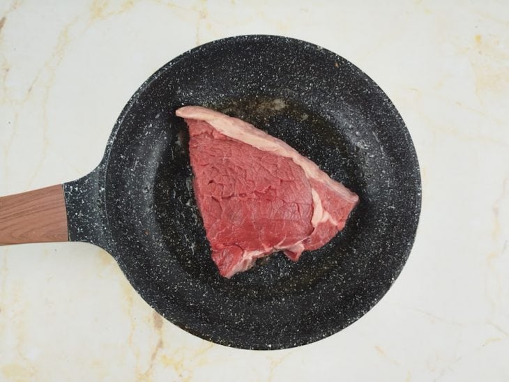 Bife sendo colocado em frigideira quente com azeite.