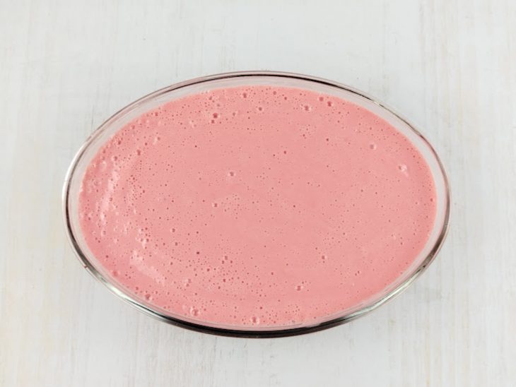 Mistura do liquidificador despejada sobre a camada de morangos.