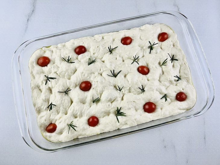 Tomates-cereja e folhas de alecrim sobre a massa.