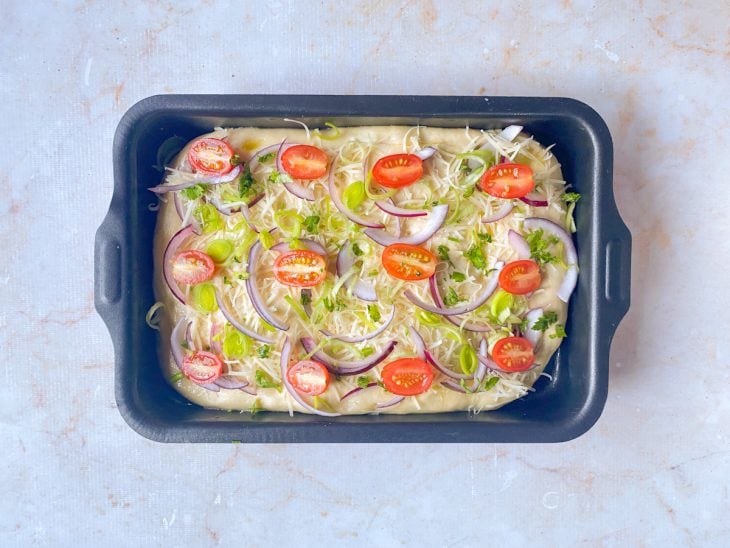 Assadeira com focaccia decorada com tomatinhos, alho-poró, cebola, queijo parmesão.