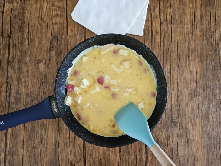 Uma frigideira com ovos, salame e queijo em cubos.