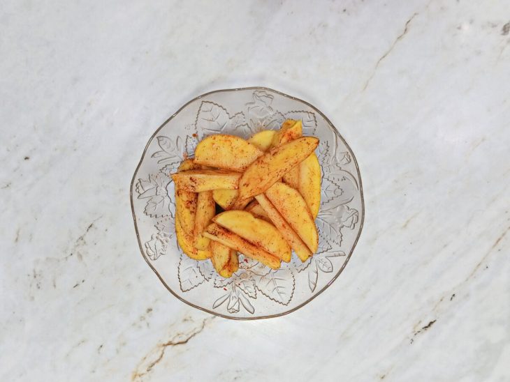 Batatas cortadas em canoas e temperadas em uma tigela.