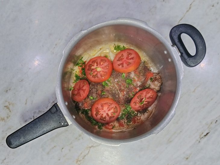 Carne retornando à panela com temperos e tomate.