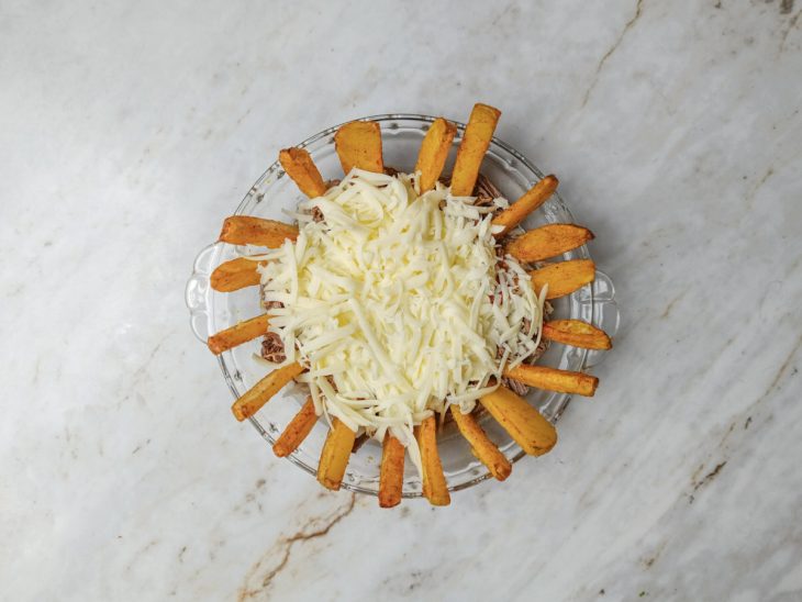 Carne desfiada regada com caldo em um refratário.