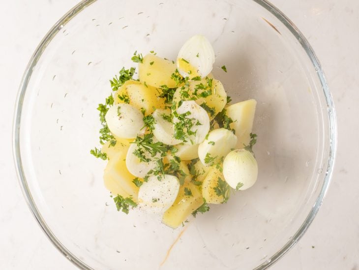 Uma tigela com as cebolas e as batatas temperadas.