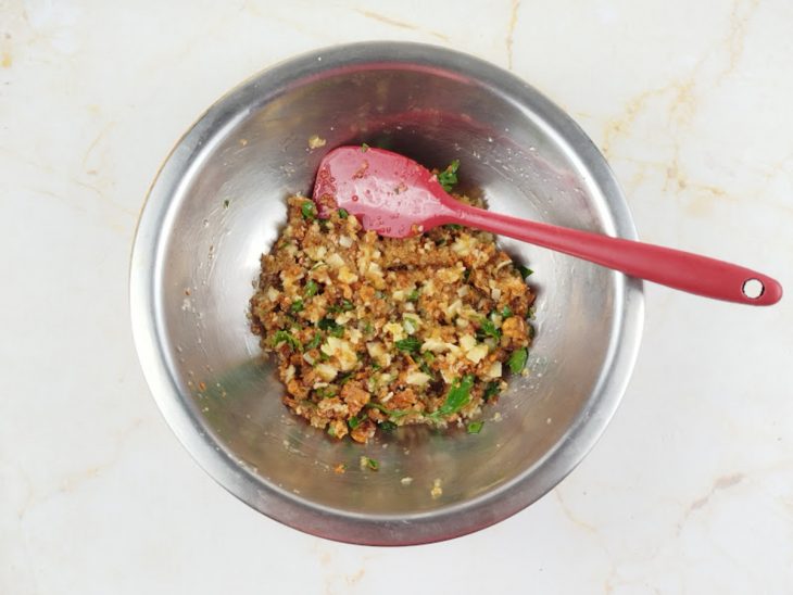 Farofa de alho, queijo, panko e salsinha misturada em tigela.