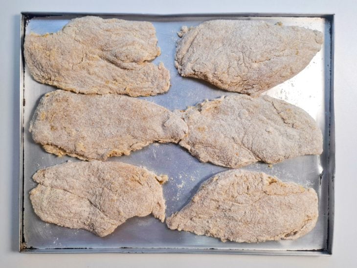 Filés de frango passados na farinha e acomodados em uma forma.