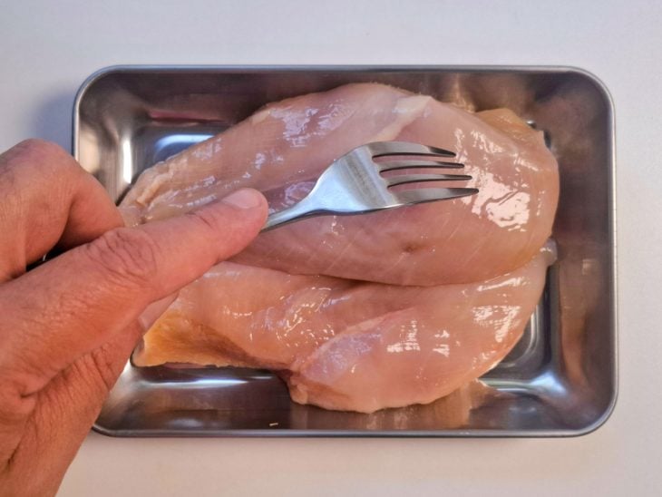 Filés de frango crus furados com garfo.