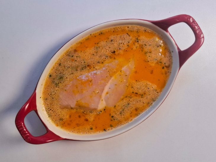 Recipiente com ovos temperados e um filé de frango.