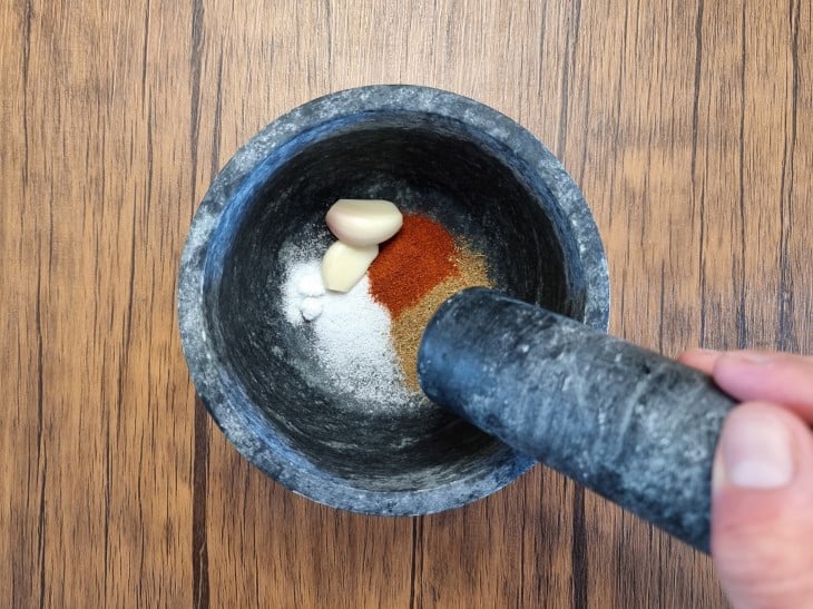 Um pilão contendo alho, sal, cominho e páprica.