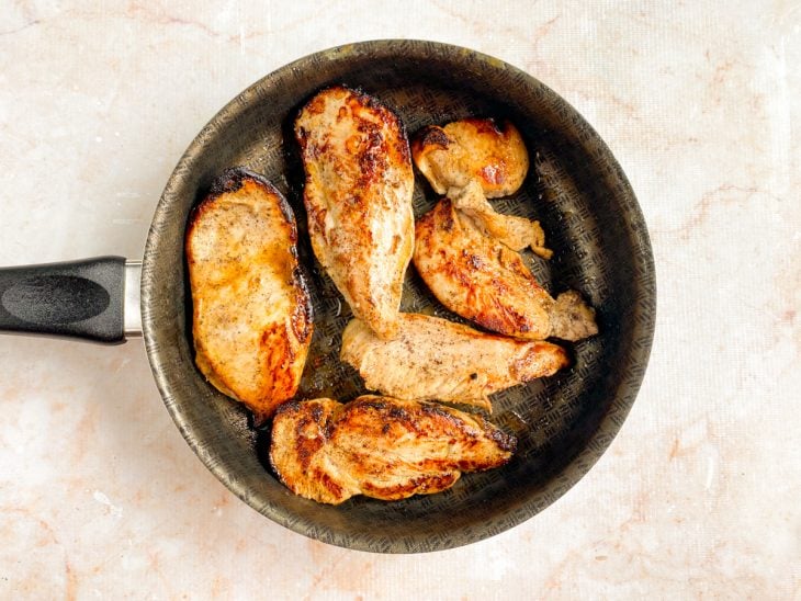 Filés de frango fritando em uma frigideira com manteiga.