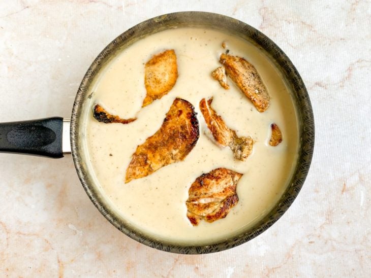 Sal, pimenta-do-reino e filés de frango adicionados a panela com molho branco.